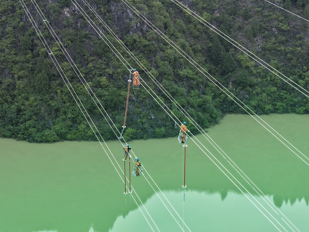 10月22日，在湖北十堰郧阳区青山镇琵琶滩村的汉江河谷，国网十堰供电公司5名施工人员攀上高空，脚踩飞车、身系安全绳沿着导线在百米高空安装避雷器、间隔棒等附件设备。工程届时将为西武高铁湖北段箭流铺、东河牵引站提供主电源。（郝金鑫 ）.jpg